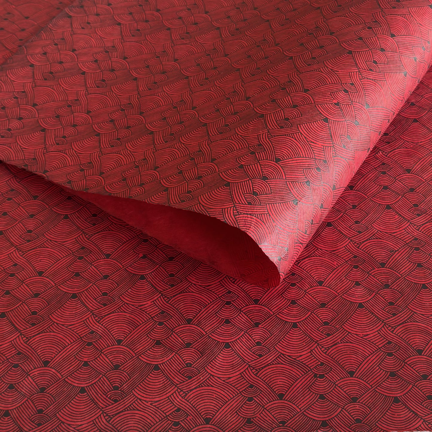Nepalese handmade decorative lokta paper sheet with a fine lined black knots pattern screen printed on a red lokta paper.