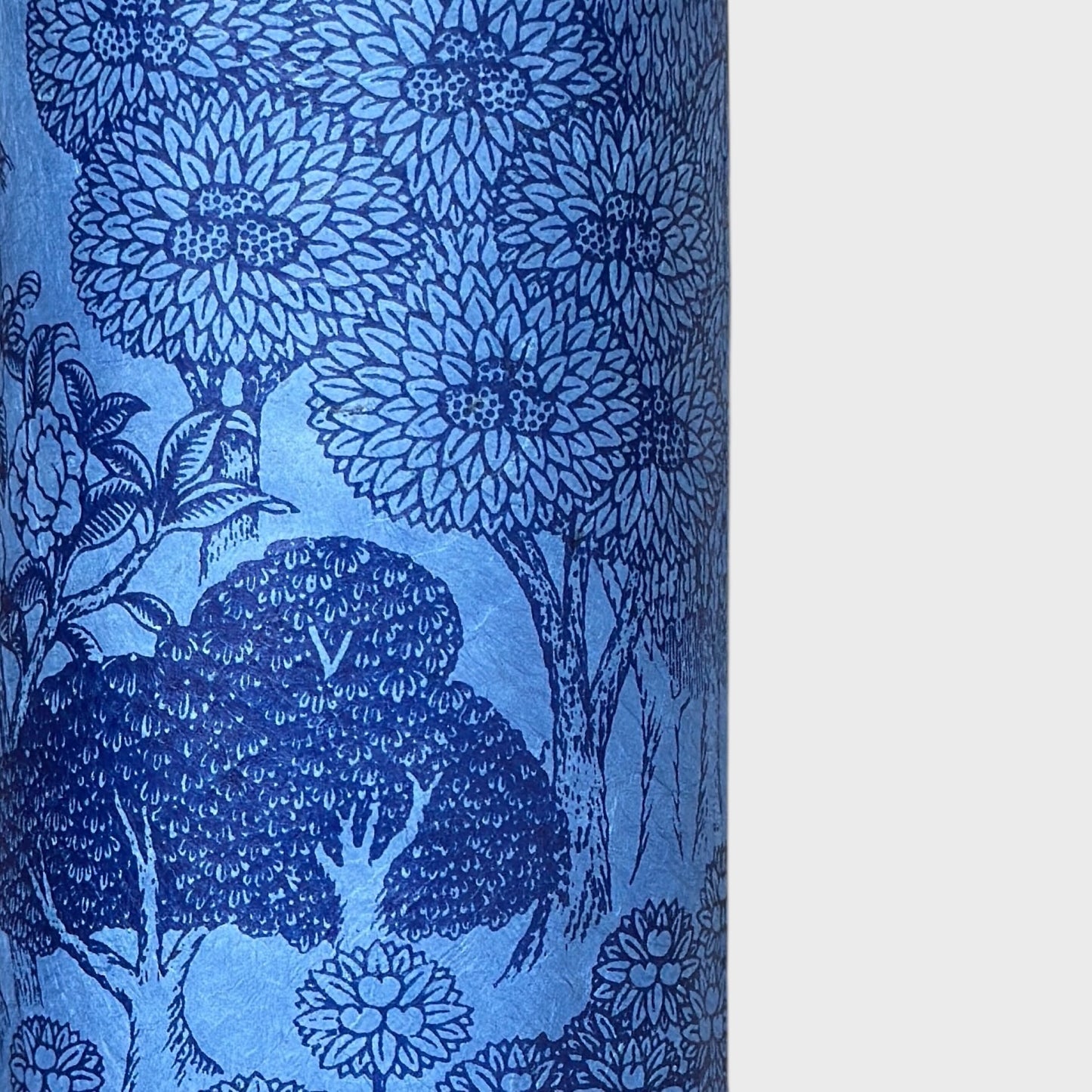 Detailed pattern of trees and flowers in dark blue screen-printed by hand on a blue lokta paper. Close up