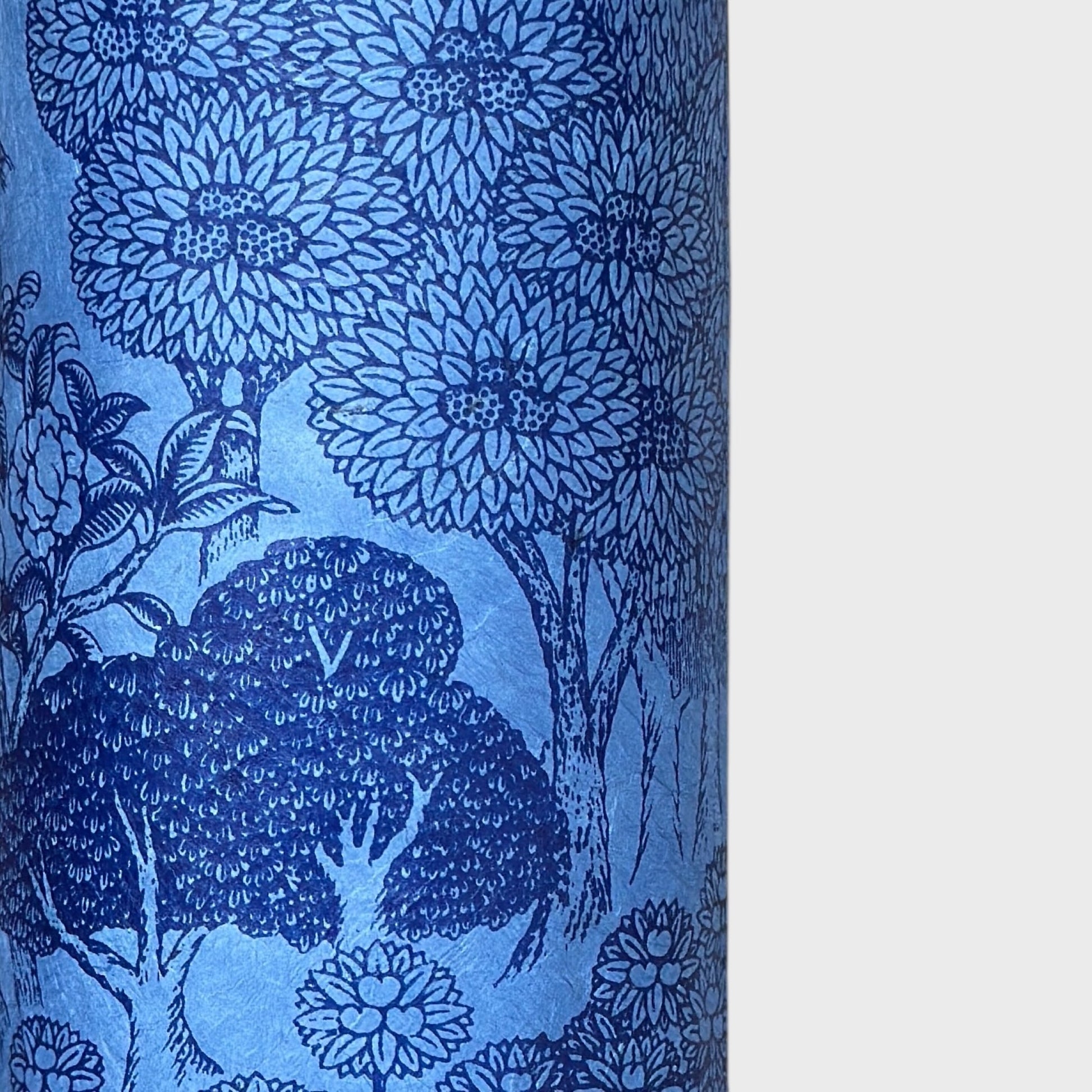 Detailed pattern of trees and flowers in dark blue screen-printed by hand on a blue lokta paper. Close up