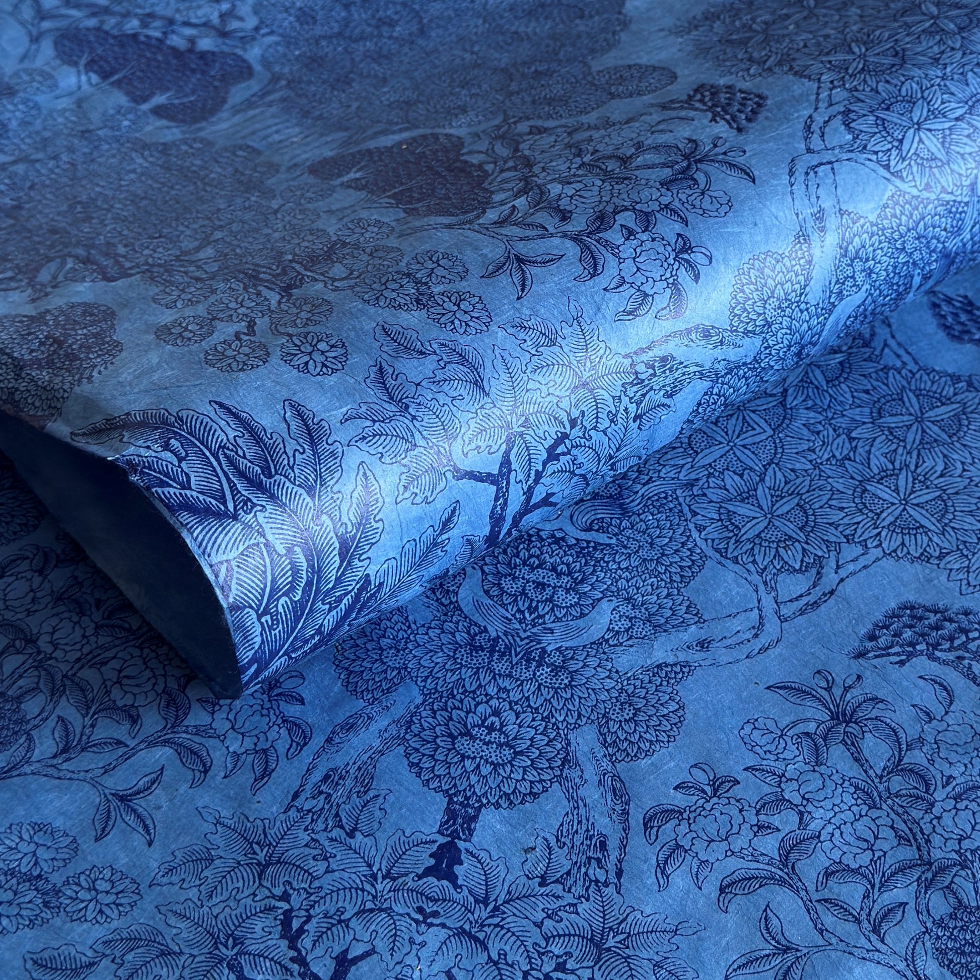 Detailed pattern of trees and flowers in dark blue screen-printed by hand on a blue lokta paper. 