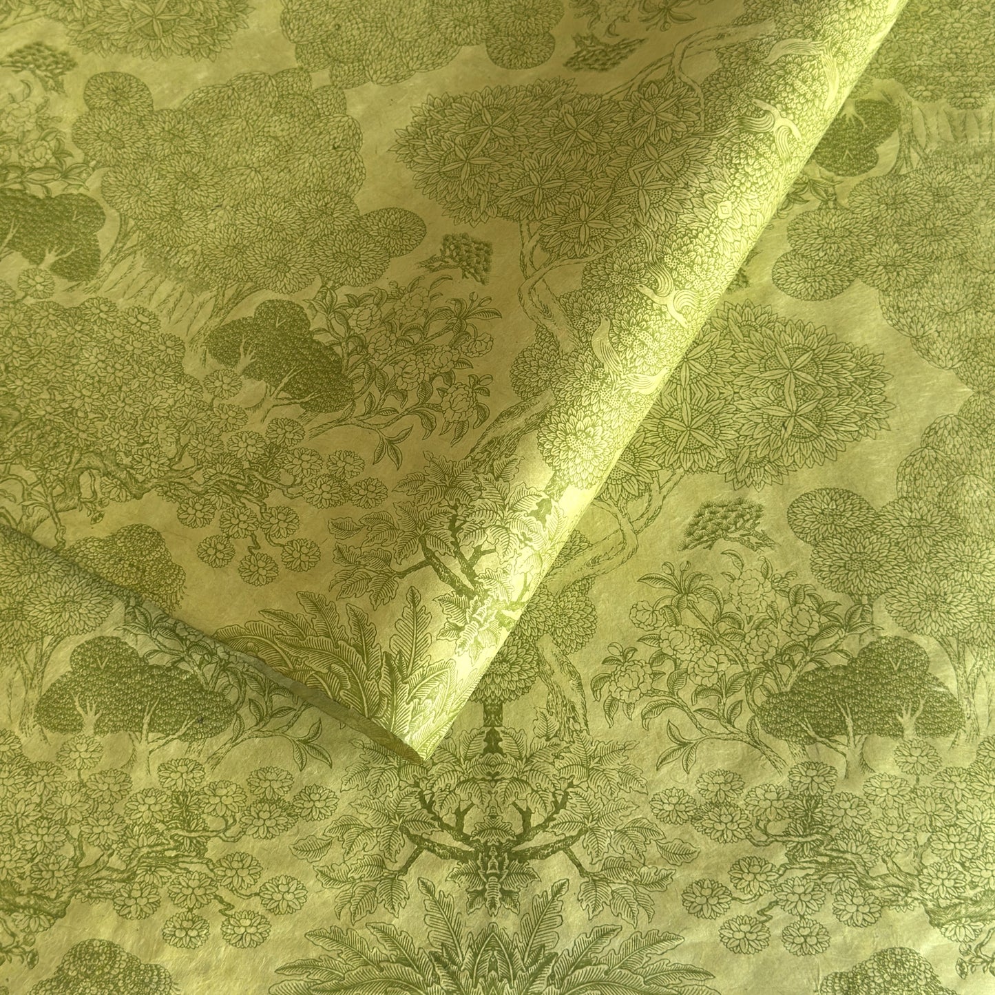 Nepalese handmade decorative lokta paper sheet with a detailed design of trees and flowers in dark green screen printed on a green lokta paper.