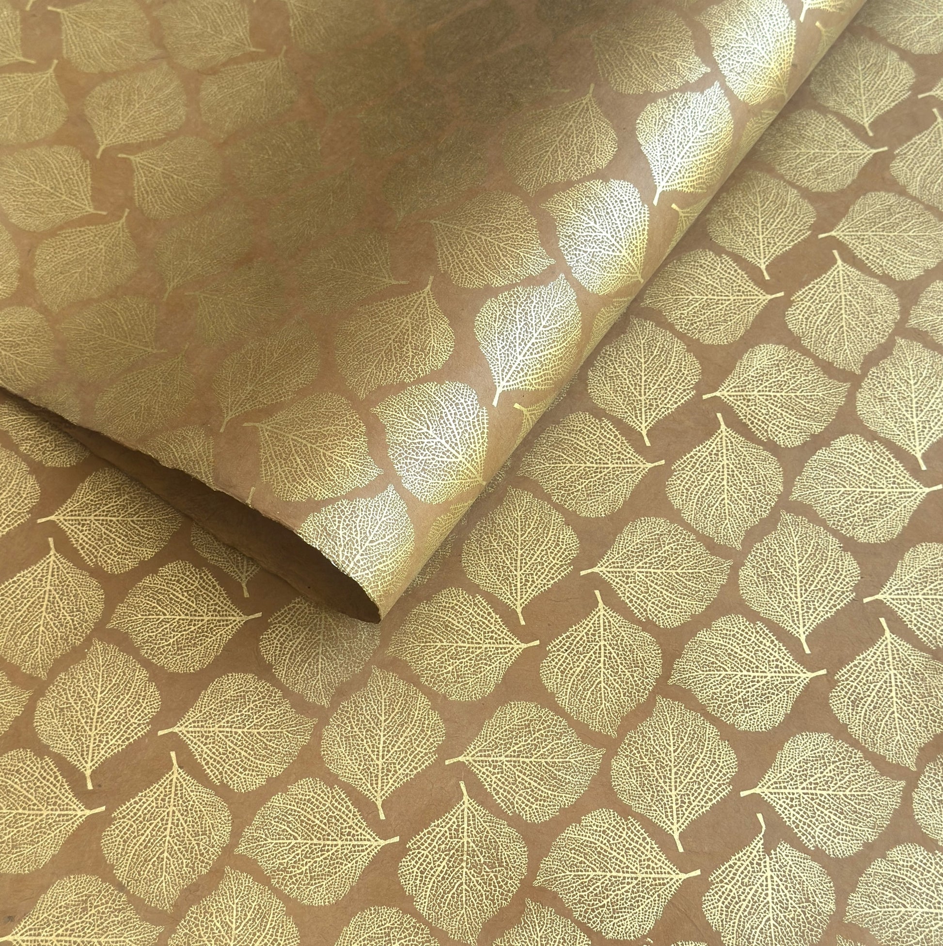 Nepalese handmade decorative lokta paper sheet with a gold metallic leaf pattern screen printed on a tan lokta paper.