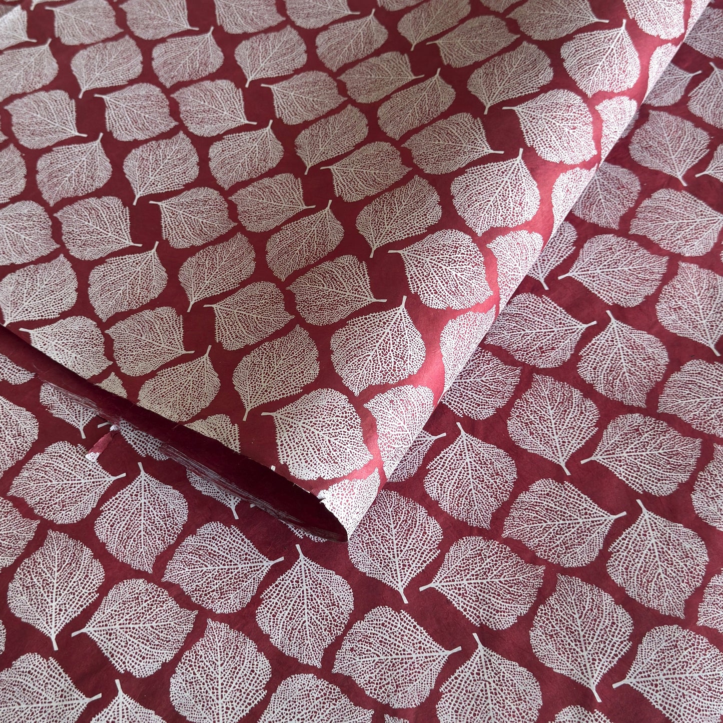 Nepalese handmade decorative lokta paper sheet with a white leaf pattern screen printed on a burgundy lokta paper.