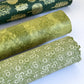 Nepalese handmade decorative lokta paper sheet with a white ditsy floral design screen printed on a green lokta paper. Pictured rolled with other designs