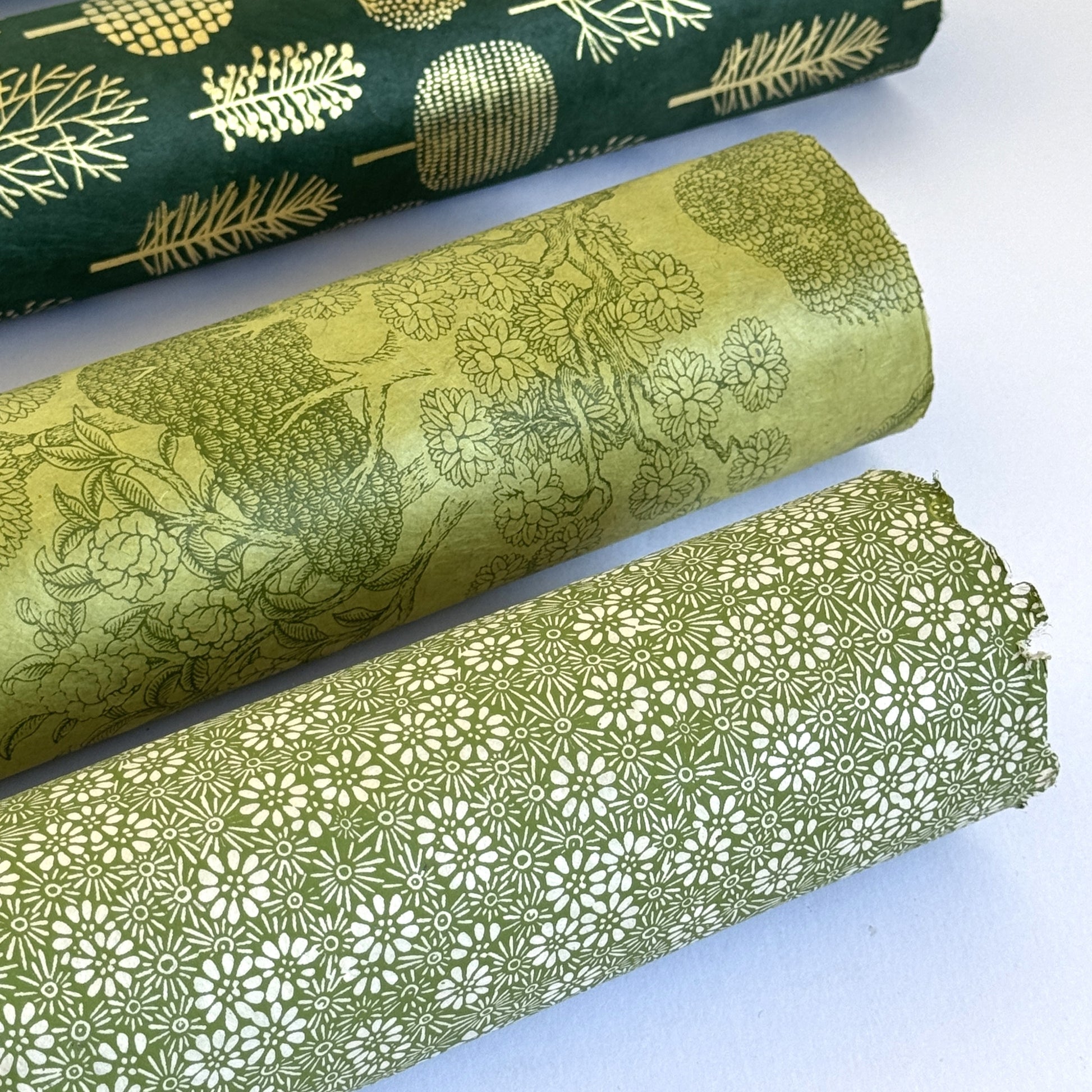 Nepalese handmade decorative lokta paper sheet with a white ditsy floral design screen printed on a green lokta paper. Pictured rolled with other designs