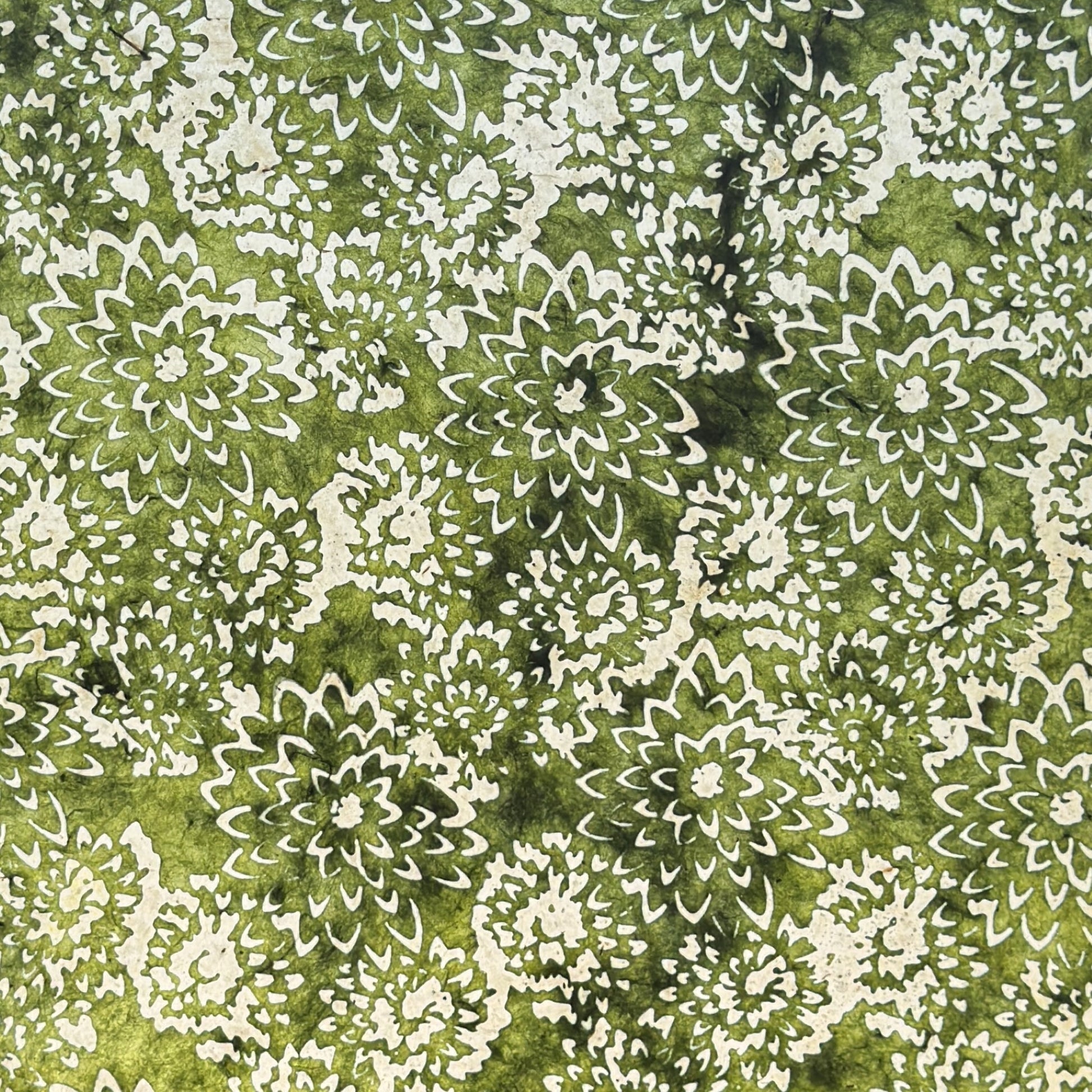 Nepalese handmade decorative lokta paper sheet with a floral pattern in green and cream.  Batik dyed using carved wooden blocks.  Photographed with light to show the translucent nature