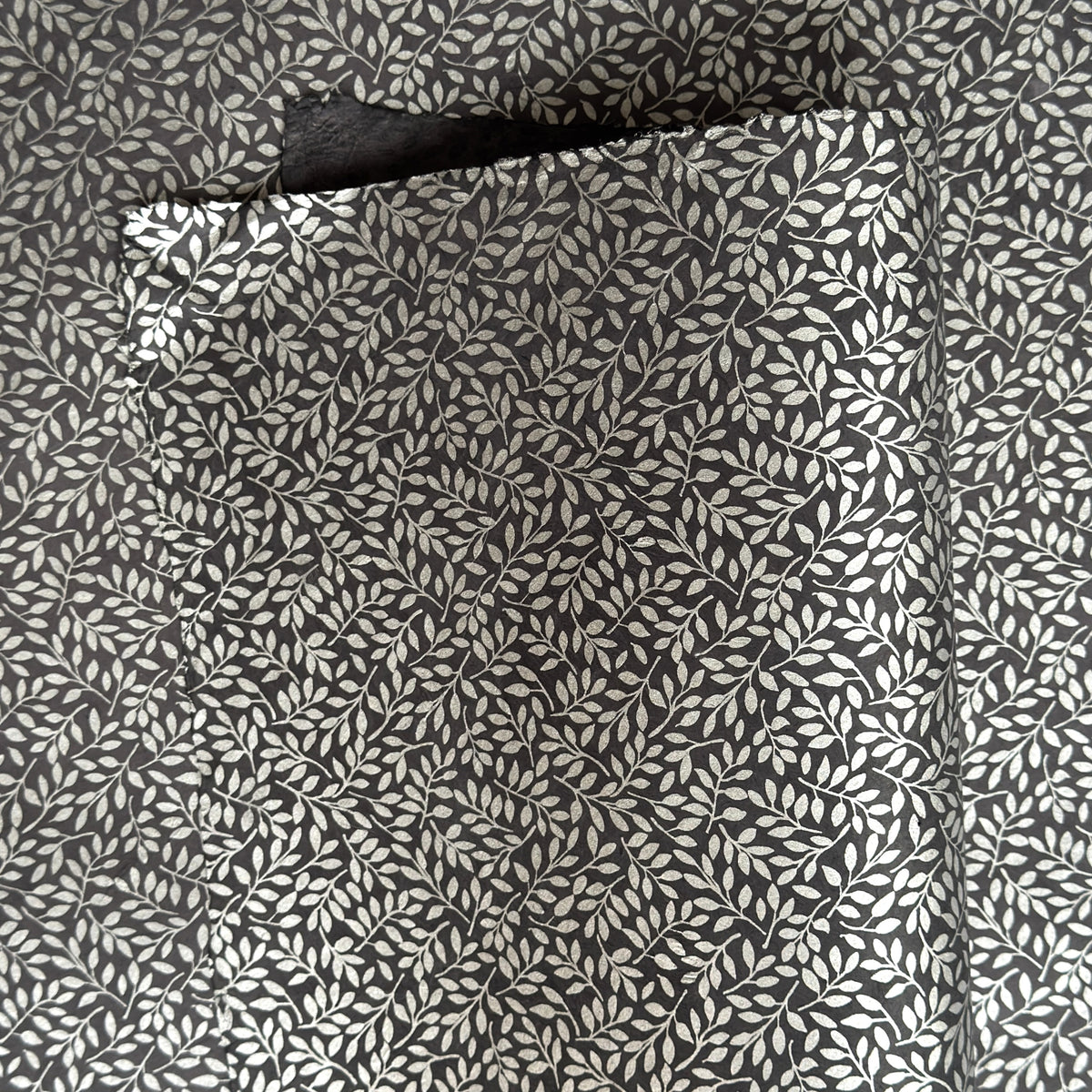 a sheet of screen printed Nepalese lokta paper with a small repeat silver leaf design on slate grey lokta paper