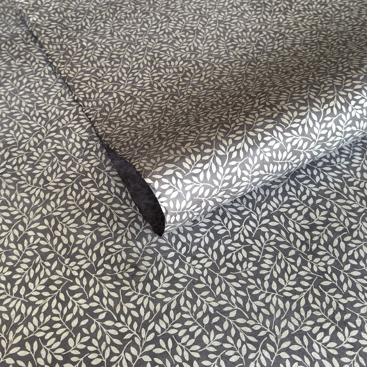 a sheet of screen printed Nepalese lokta paper with a small repeat silver leaf design on slate grey lokta paper