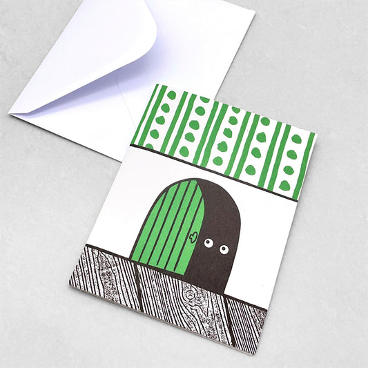 Small greetings card of a semi-circle green door in the skirting board, the door is slightly open showing two eyes of the mouse that lives there. Above the skirting is green and white stripe/dot wallpaper by Lisa Jones Studio