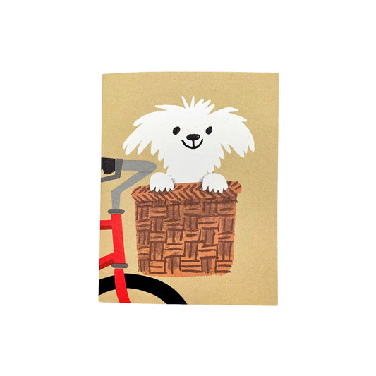 Small greetings card with a drawing of a happy white dog in the basket of a red bike, with beige backdrop by Lisa jones Studio