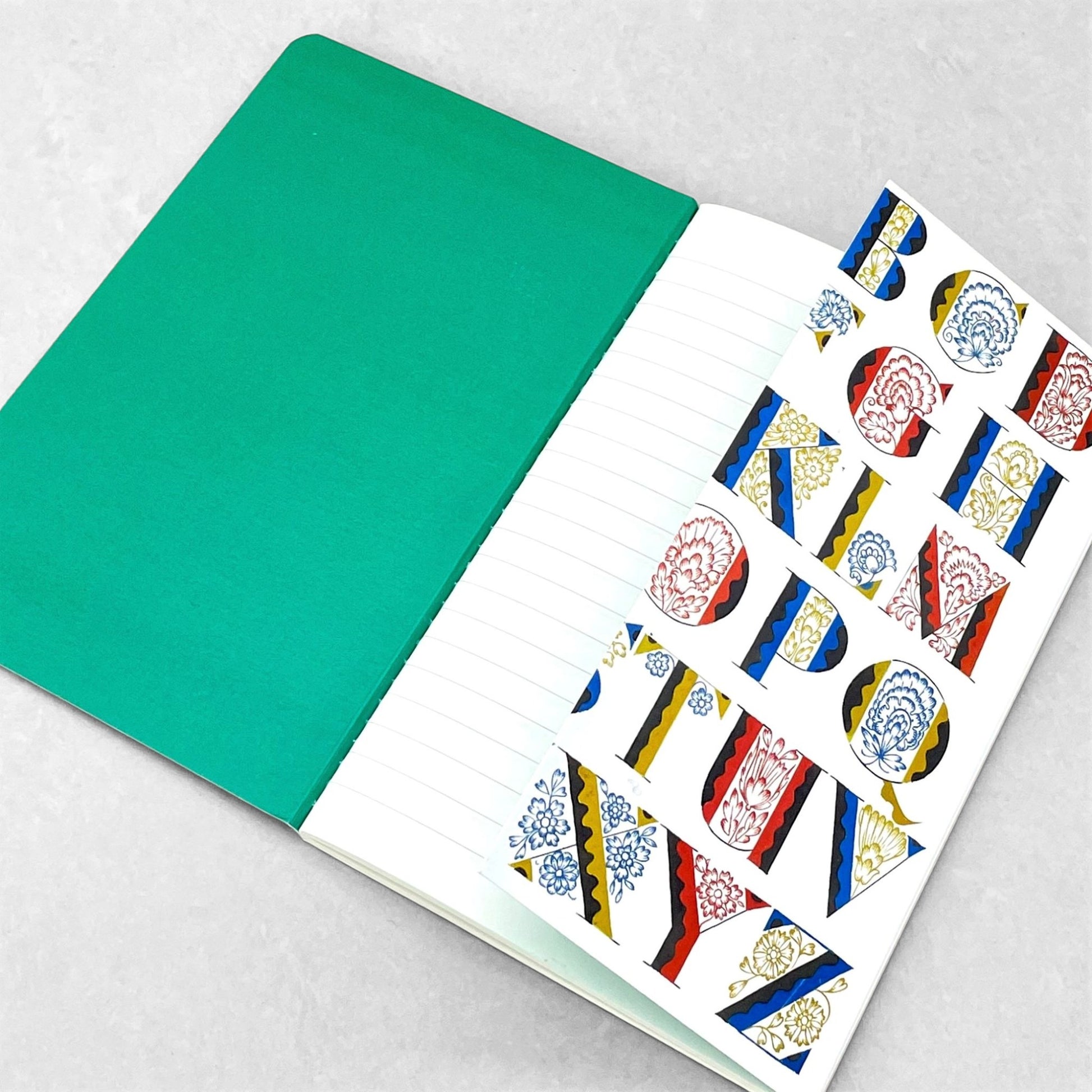 Small stitched notebook with a colourful alphabet cover design in red, blue and yellow on white background