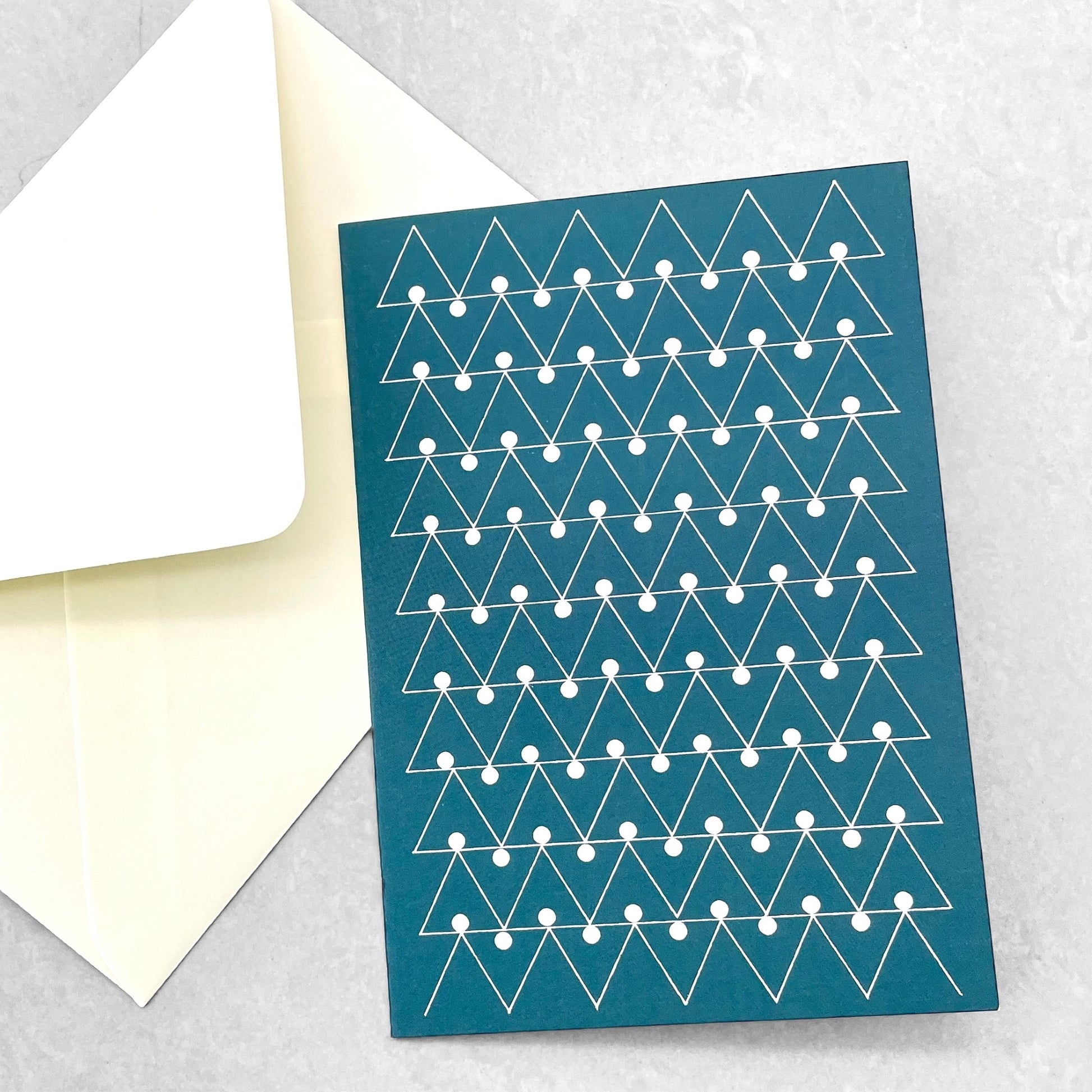 Greetings card by Ola Studio with a triangular geometric design in white on a deep teal background, with envelope