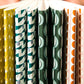 slimline softcover exercise book by Ola Studio, with plain pages. Front cover is a wavy stripe design in dark green and aqua on white. Pictured with other notebook designs from the collection