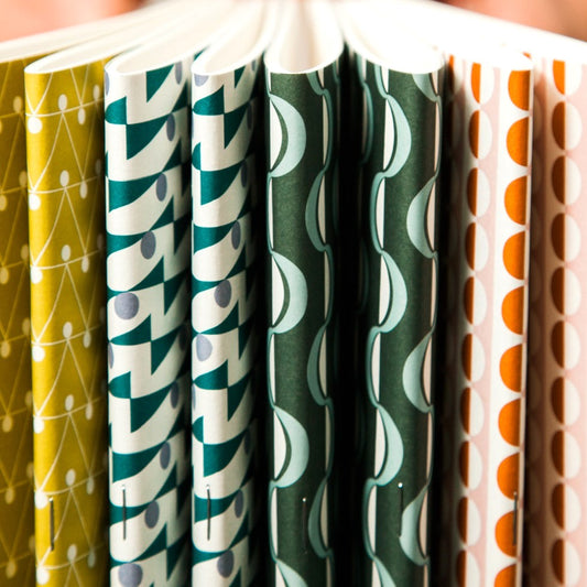Slimline, softcover exercise book by Ola Studio with a triangular geometric cover in mustard and white, pictured with other designs from the collection