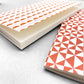 A set of two softcover pocket notebooks by Ola Studio. Two different cover design, one is a circle geometric in pick and orange, the other a triangular geometry in brick red. close up of plain white pages