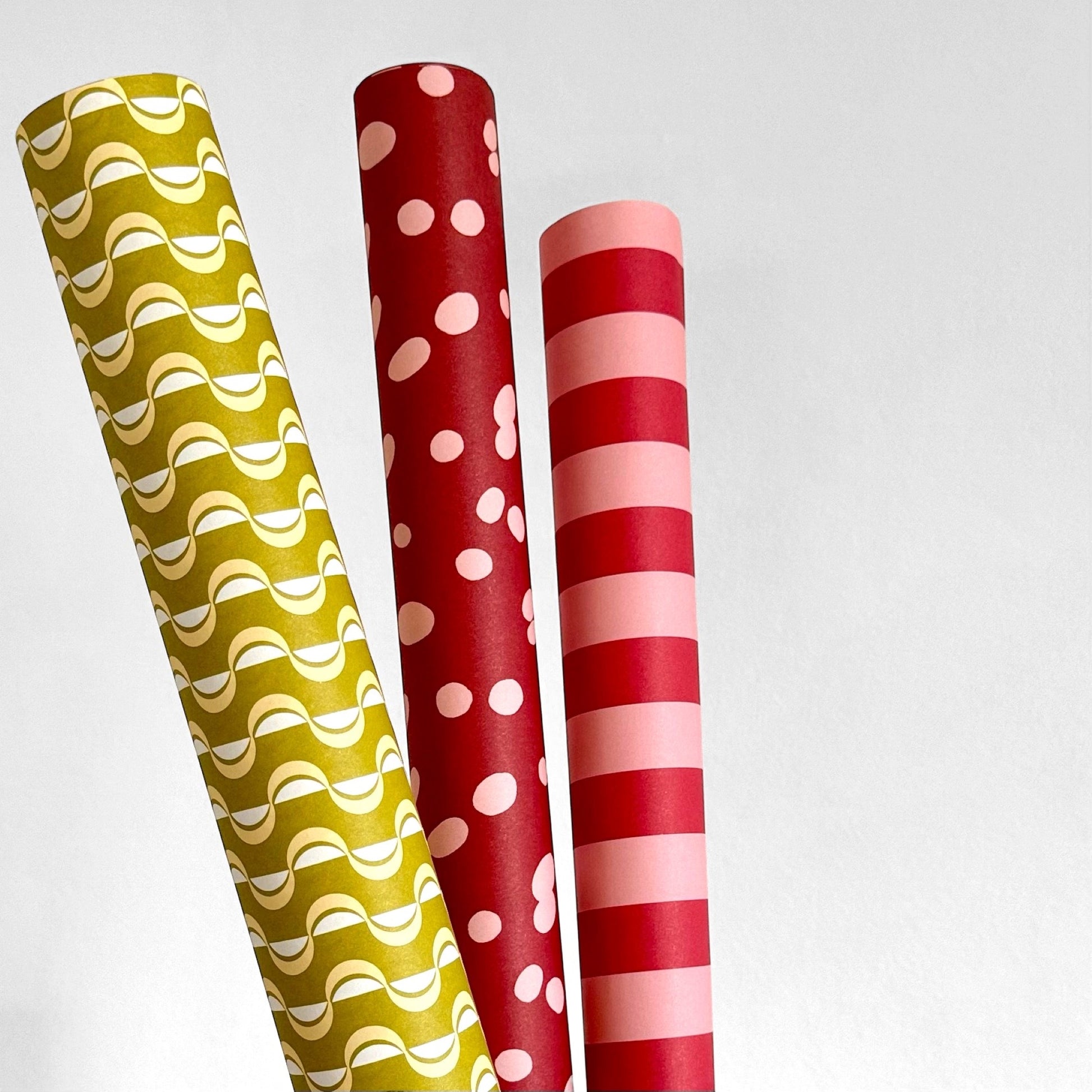 wrapping paper by ola studio with a wavy stripe design in chartreuse and lemon. Pictured rolled alongside red patterned papers.