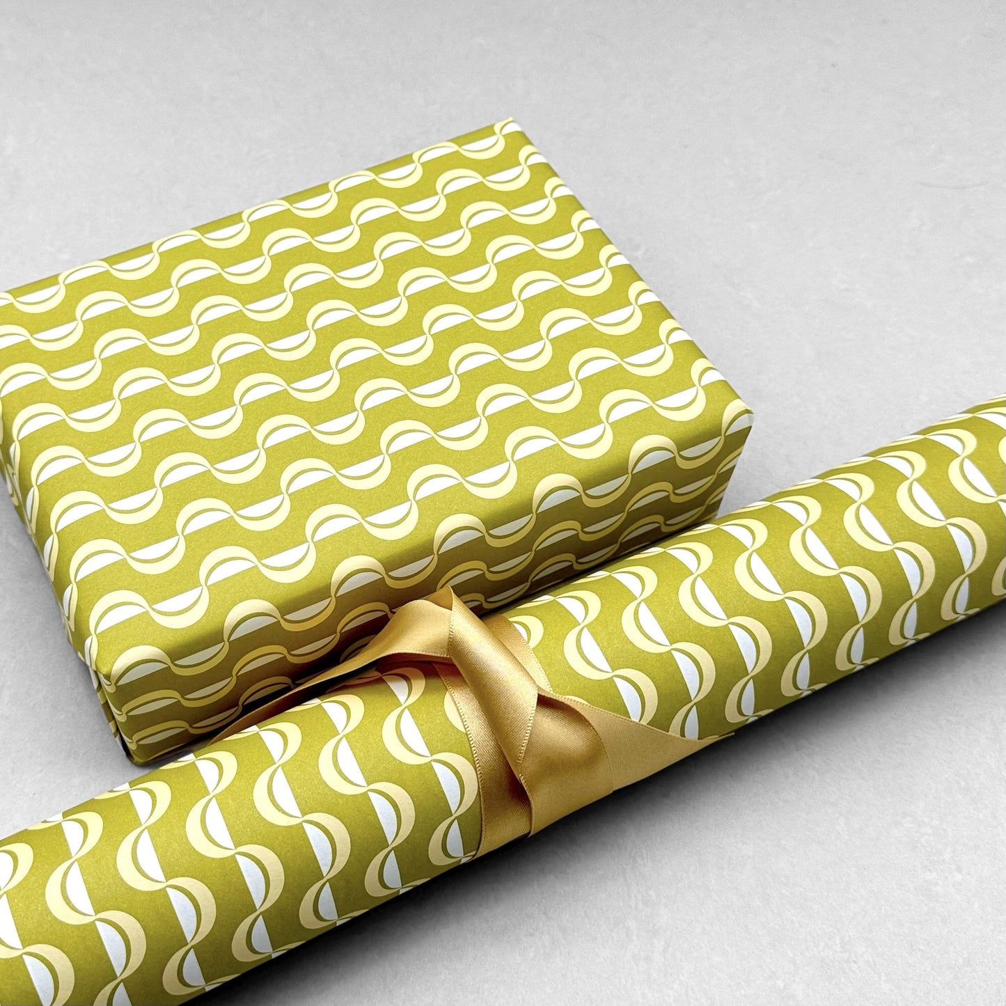 wrapping paper by ola studio with a wavy stripe design in chartreuse and lemon. Pictured wrapped with a roll of the paper alongside.