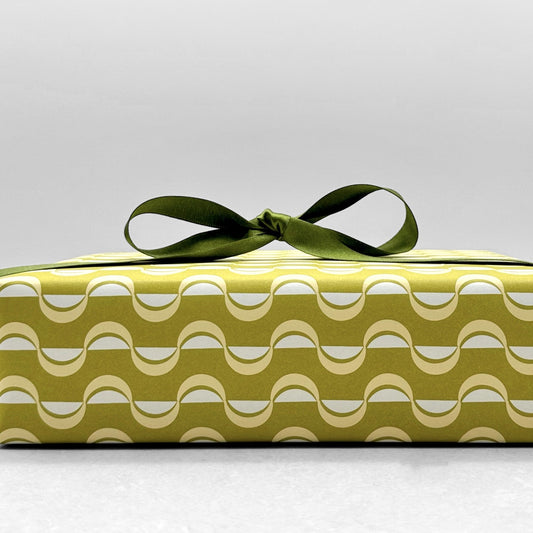 wrapping paper by ola studio with a wavy stripe design in chartreuse and lemon. Pictured wrapped with a green satin ribbon