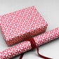 wrapping paper by Otto Editions with a cut-out flower design in white on a magenta pink background. Pictured wrapped as a present with a roll of the paper