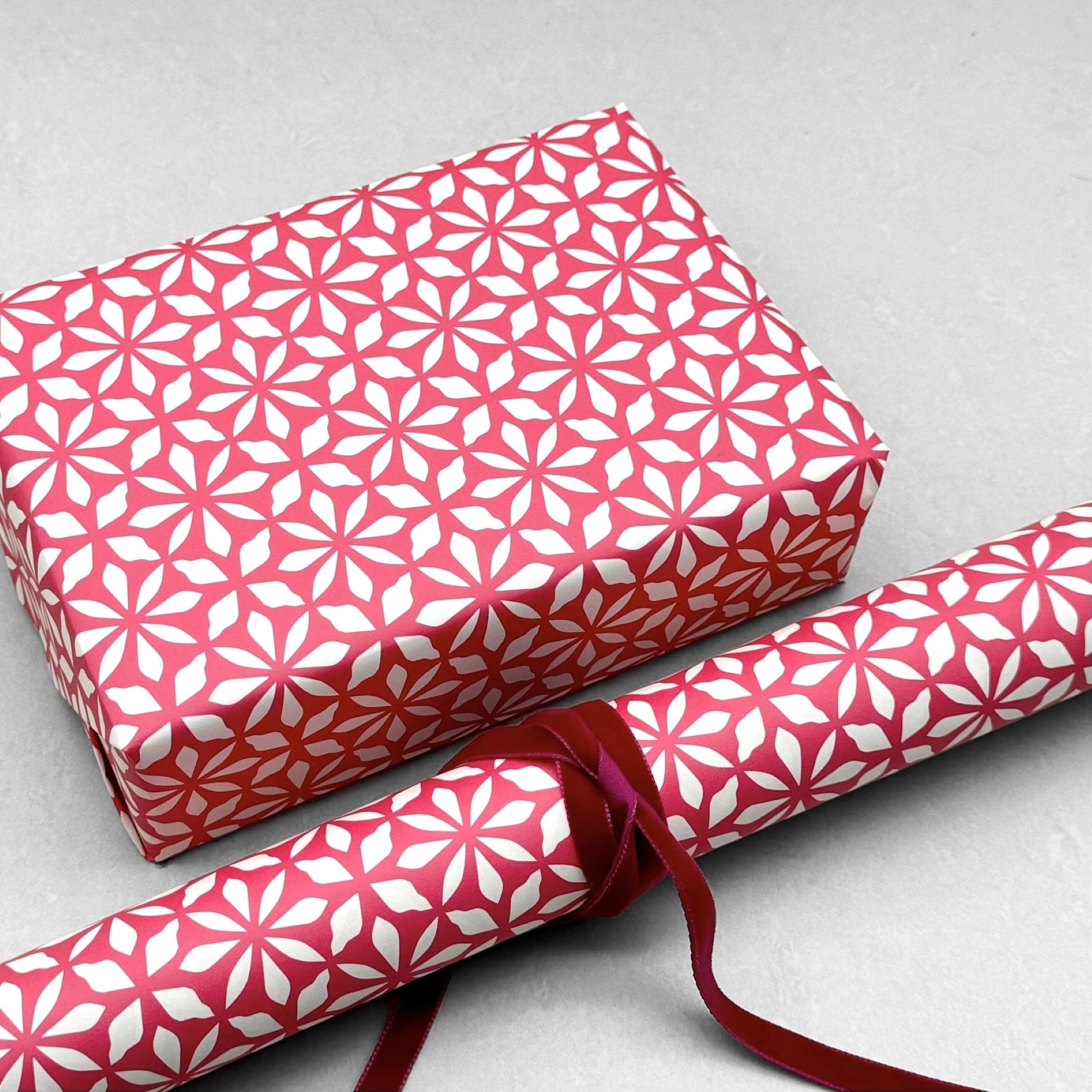 wrapping paper by Otto Editions with a cut-out flower design in white on a magenta pink background. Pictured wrapped as a present with a roll of the paper