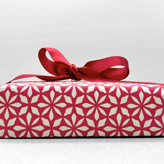 wrapping paper by Otto Editions with a cut-out flower design in white on a magenta pink background. Pictured wrapped as a present with a red bow