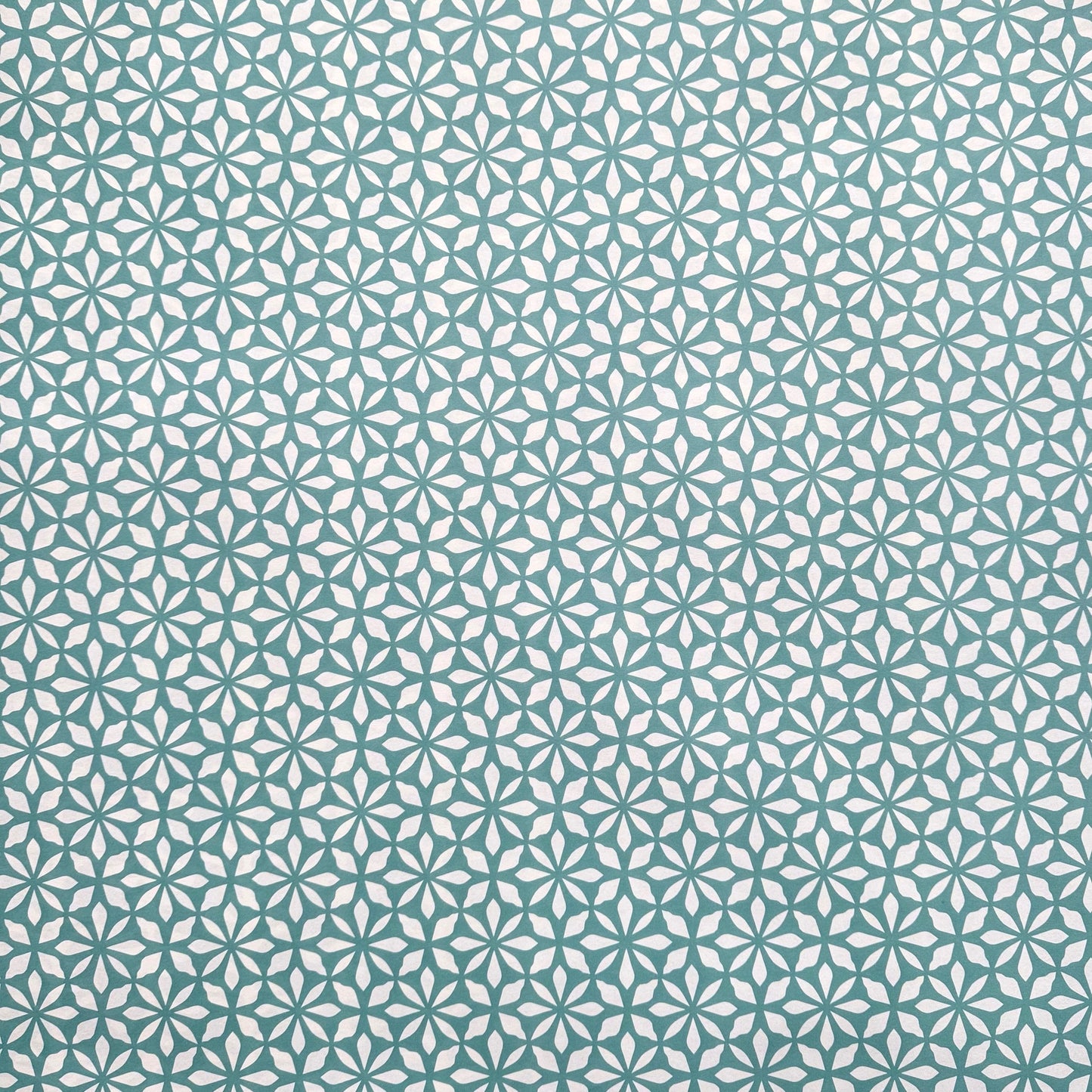 wrapping paper by Otto Editions with a cut-out flower design in white on an aqua blue background. 