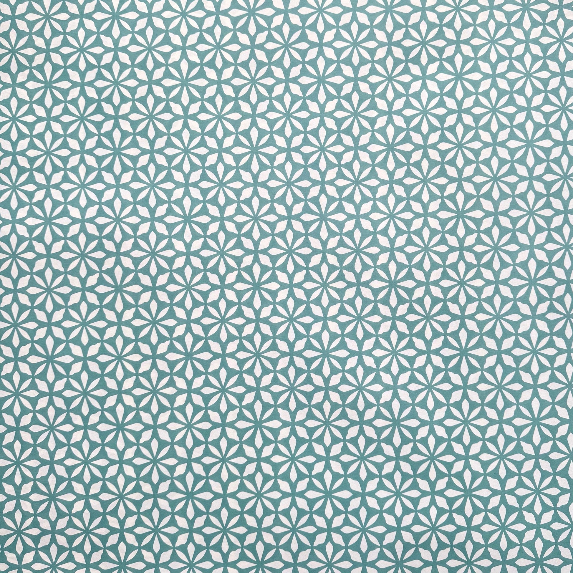 wrapping paper by Otto Editions with a cut-out flower design in white on an aqua blue background. 