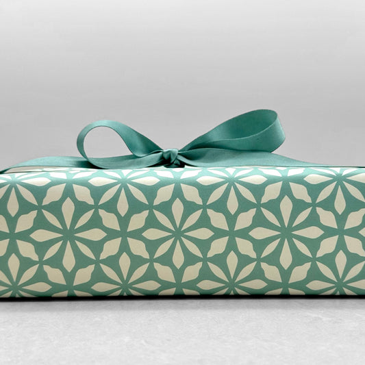 wrapping paper by Otto Editions with a cut-out flower design in white on an aqua blue background. Pictured wrapped as a present with an aqua bow