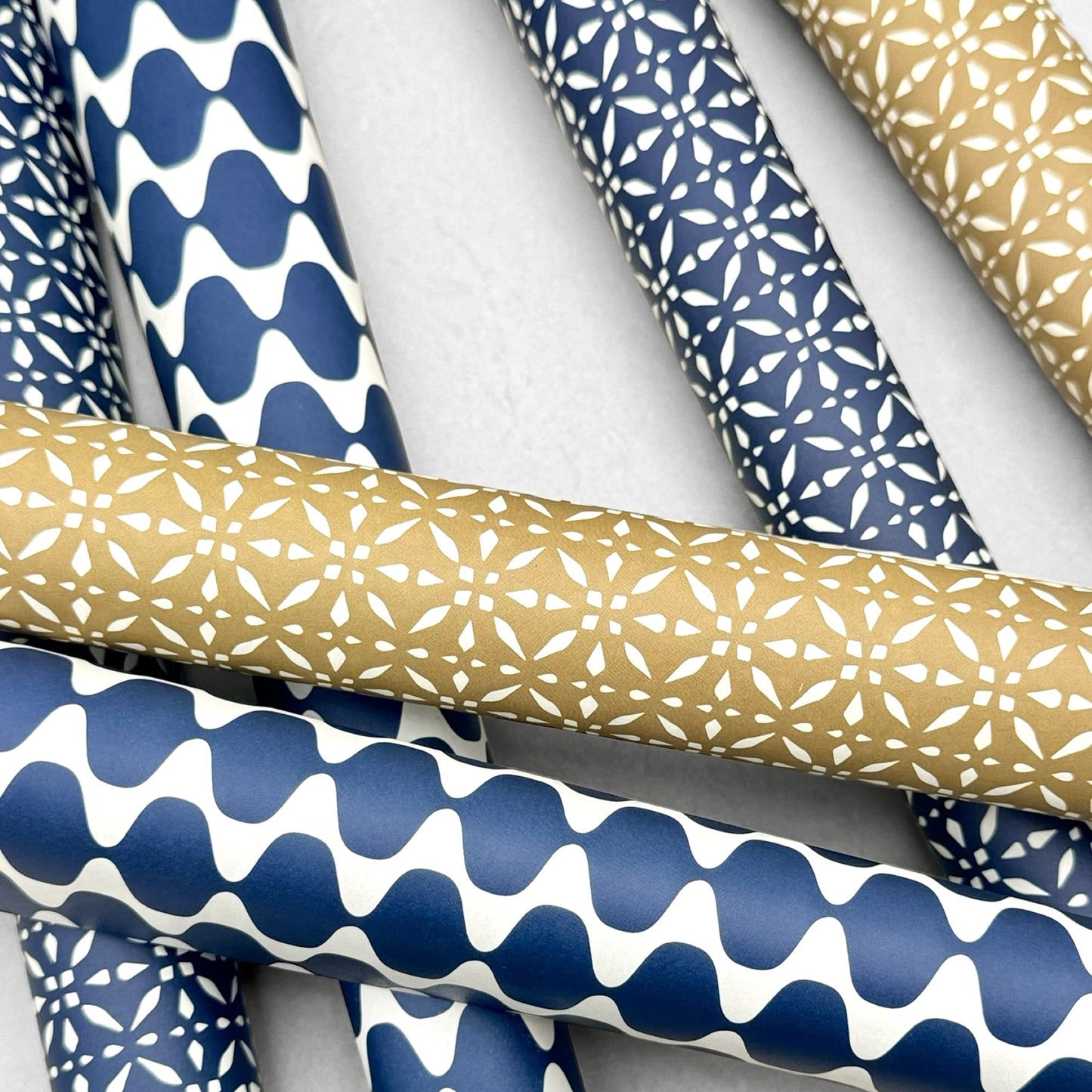 wrapping paper by Otto Editions with a cut-out design in white on a gold background. Pictured rolled alongside other designs