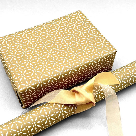 wrapping paper by Otto Editions with a cut-out design in white on a gold background. Pictured wrapped as a present with a roll of the paper