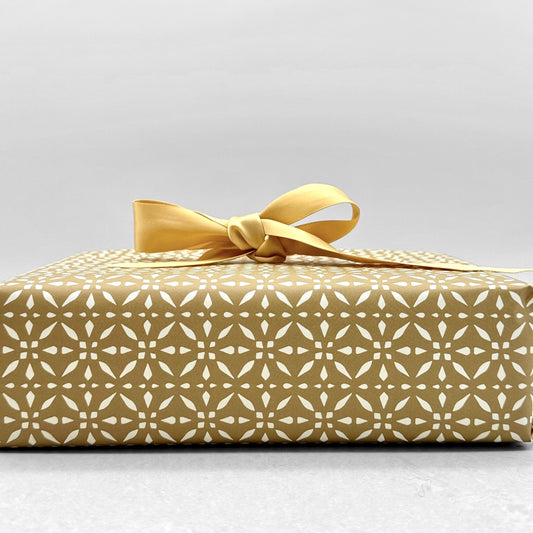 wrapping paper by Otto Editions with a cut-out design in white on a gold background. Pictured wrapped as a present with a gold bow