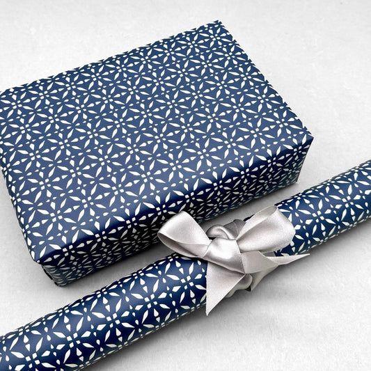 wrapping paper by Otto Editions with a cut-out design in white on an indigo blue background. Pictured wrapped as a present with a roll of the paper