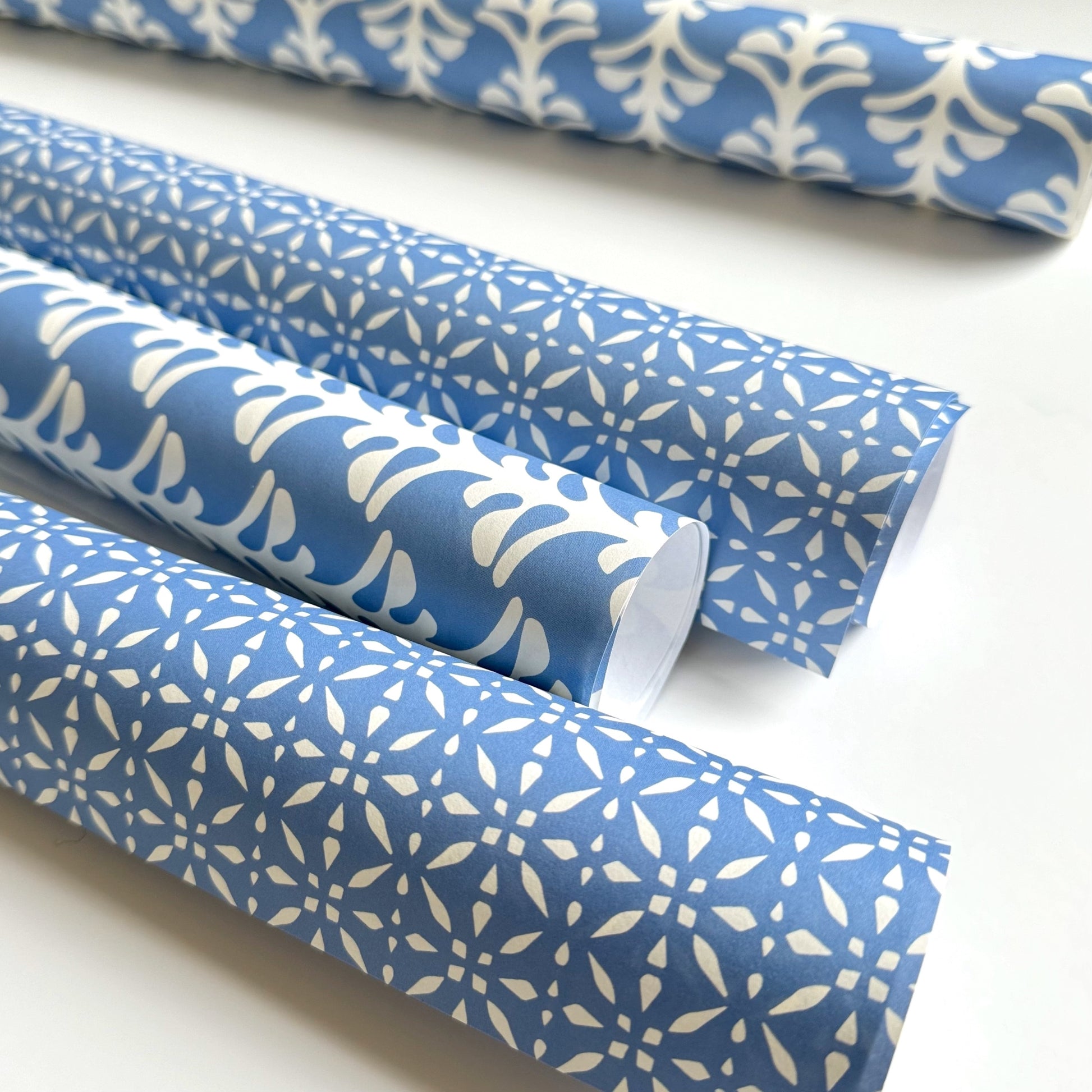 wrapping paper by Otto Editions with a cut-out design in white on a sky blue background. Pictured rolled alongside other designs