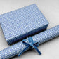 wrapping paper by Otto Editions with a cut-out design in white on a sky blue background. Pictured wrapped as a present with a roll of the paper