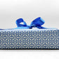 wrapping paper by Otto Editions with a cut-out design in white on a sky blue background. Pictured wrapped as a present with a blue bow