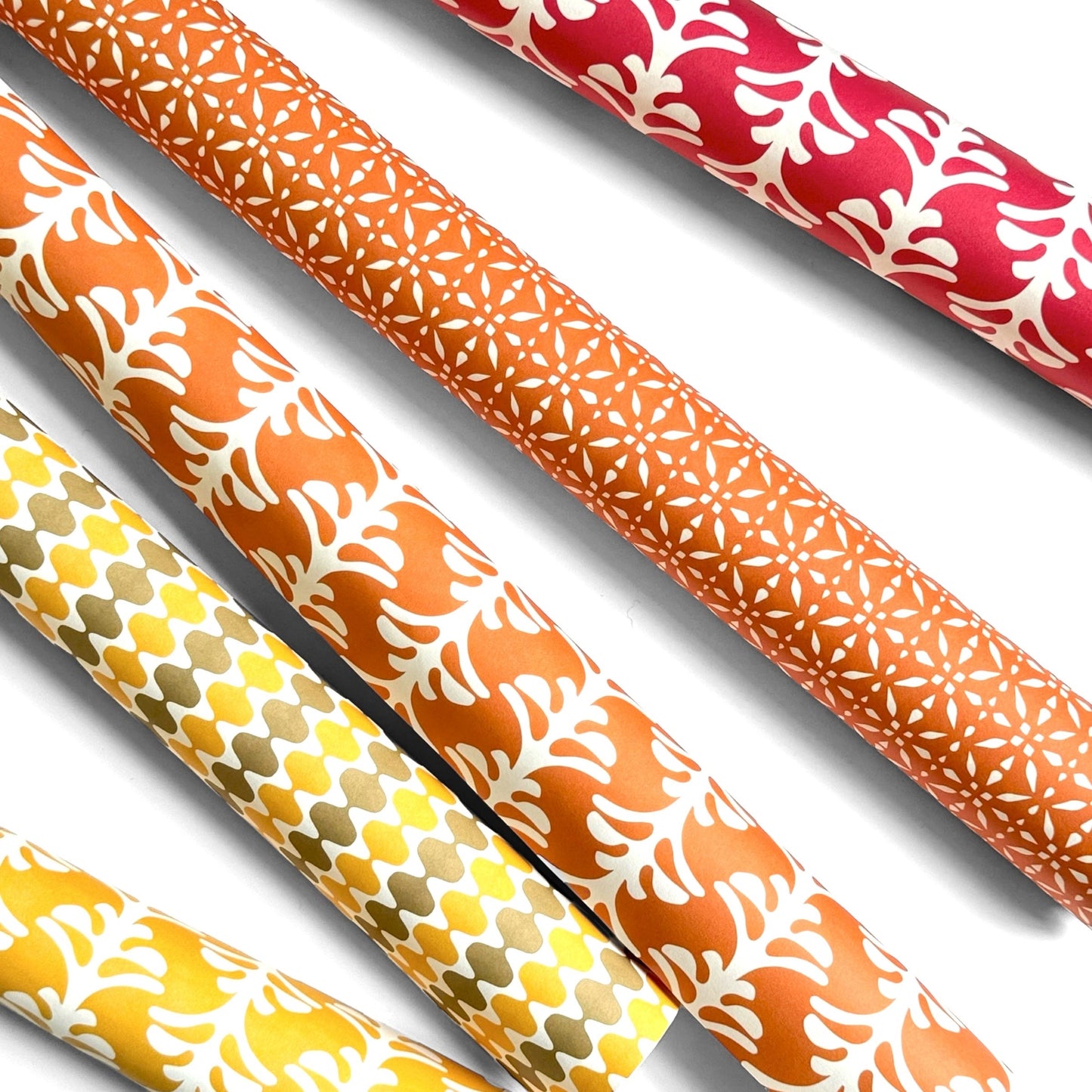 wrapping paper by Otto Editions with a cut-out design in white on a spice orange background. Pictured rolled alongside other designs