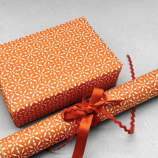 wrapping paper by Otto Editions with a cut-out design in white on a spice orange background. Pictured wrapped as a present with a roll of the paper