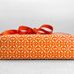 wrapping paper by Otto Editions with a cut-out design in white on a spice orange background. Pictured wrapped as a present with a bow