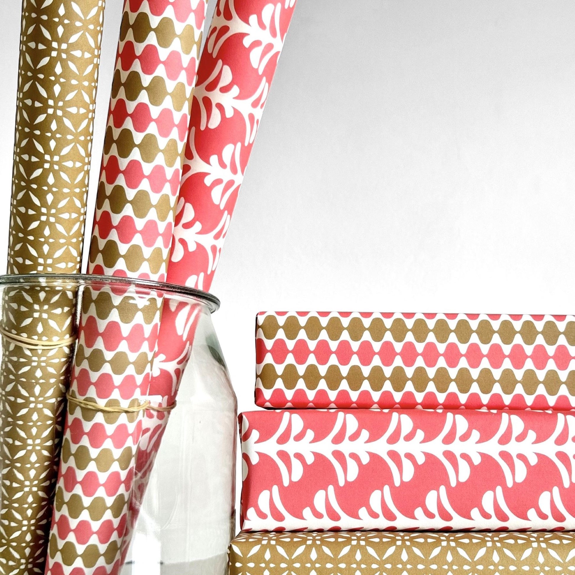 wrapping paper by Otto Editions with a cut-out palm design in white on a coral pink background. Pictured wrapped as a present alongside other designs