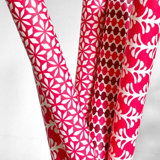 wrapping paper by Otto Editions with a cut-out flower design in white on a magenta pink background. Pictured wrapped rolled alongside other designs