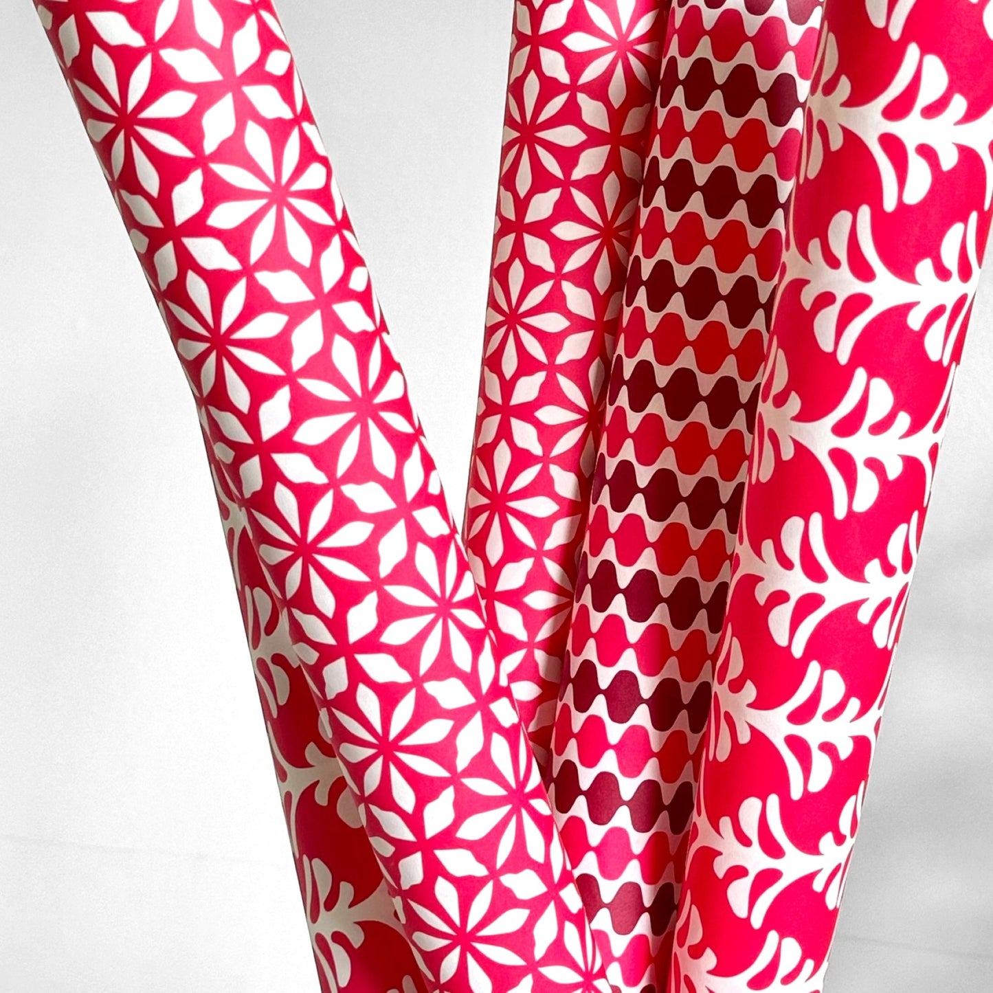 wrapping paper by Otto Editions with a cut-out palm design in white on a hibiscus pink background. Pictured rolled alongside other designs