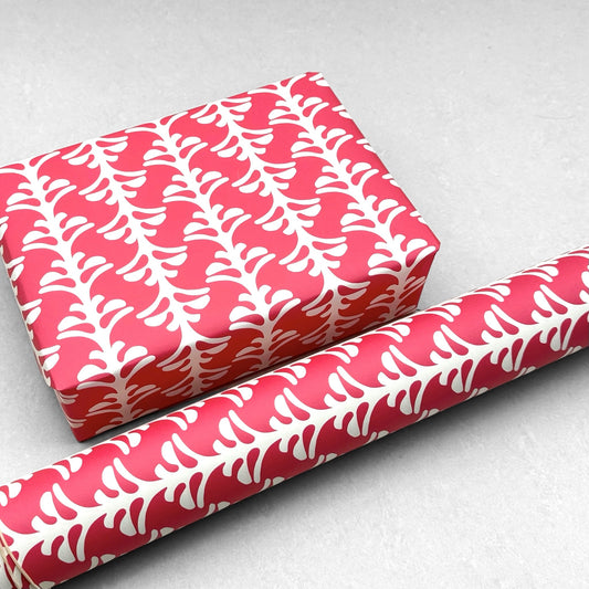 wrapping paper by Otto Editions with a cut-out palm design in white on a hibiscus pink background. Pictured wrapped as a present with a roll of the paper
