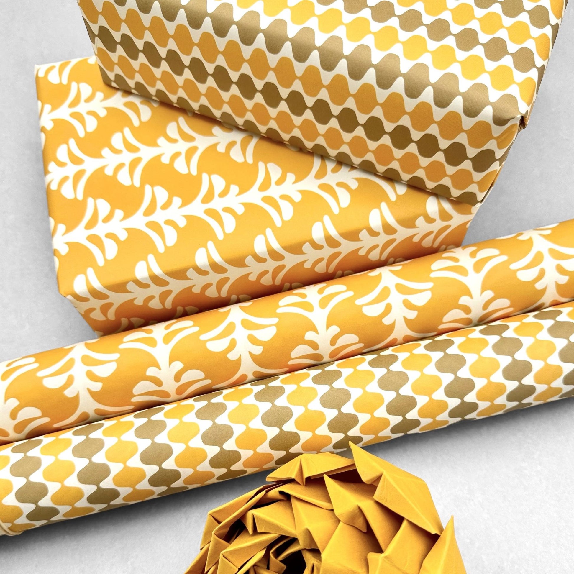 wrapping paper by Otto Editions with a cut-out palm design in white on a saffron yellow background. Pictured wrapped as a present with other designs