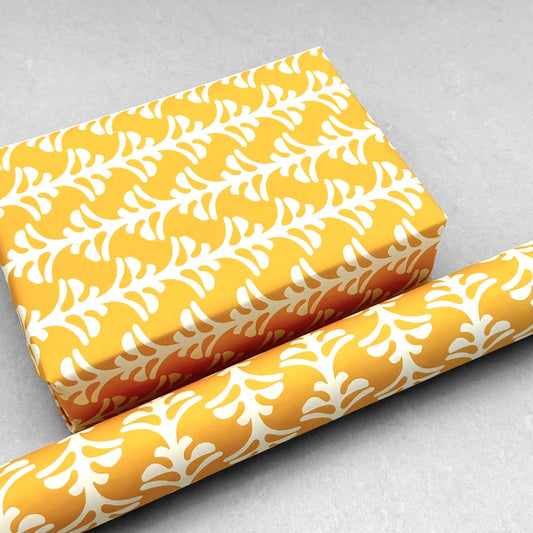 wrapping paper by Otto Editions with a cut-out palm design in white on a saffron yellow background. Pictured wrapped as a present with a roll of the paper