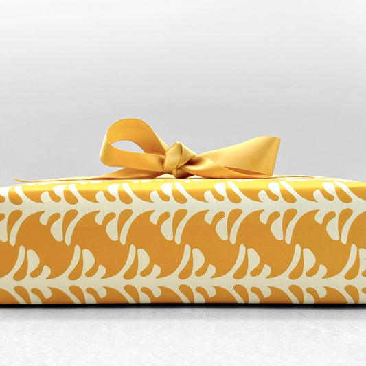 wrapping paper by Otto Editions with a cut-out palm design in white on a saffron yellow background. Pictured wrapped as a present with a yellow ribbon