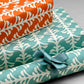 wrapping paper by Otto Editions with a cut-out palm design in white on an aqua blue background. Pictured wrapped as a present with other designs