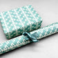 wrapping paper by Otto Editions with a cut-out palm design in white on an aqua blue background. Pictured wrapped as a present with a roll of the paper