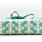 wrapping paper by Otto Editions with a cut-out palm design in white on an aqua blue background. Pictured wrapped as a present with an aqua ribbon