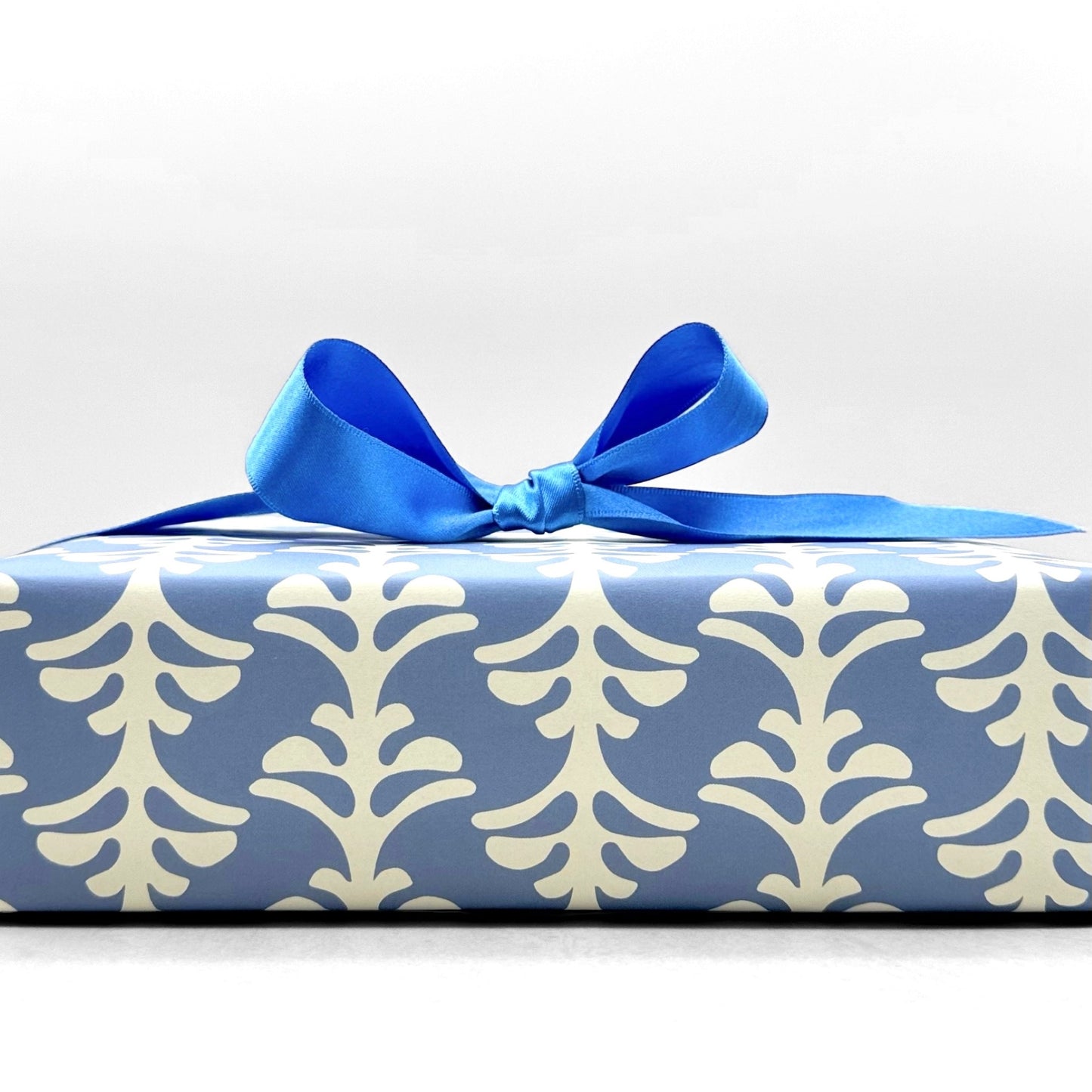 wrapping paper by Otto Editions with a cut-out palm design in white on a sky blue background. Pictured wrapped as a present with a blue ribbon