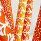 wrapping paper by Otto Editions with a cut-out palm design in white on a spice orange background. Pictured rolled with other designs